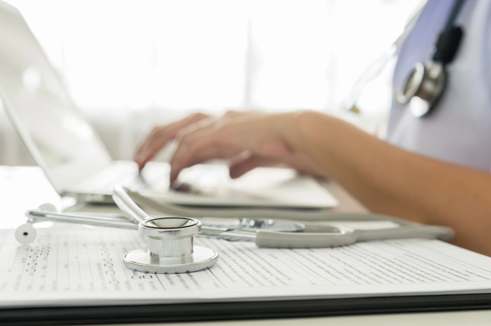 A person typing on a laptop with a stethoscope around it.